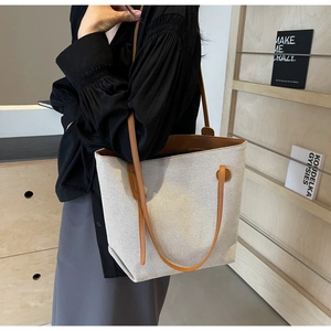 Detail of off-white canvas tote bag with brown leather handles and textured trim