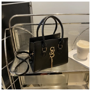 Detail of black leather handbag with golden double S logo and stylish tassel on top