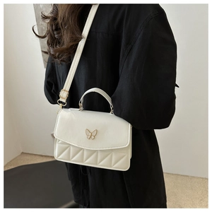 Detailed view of white quilted crossbody bag with gold butterfly clasp and slim shoulder strap