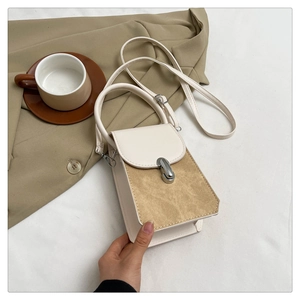 Detail of minimalist beige and brown patchwork handbag with silver clasp held by hand