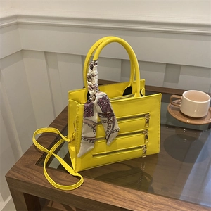 Detail of yellow handbag with gold zippers, silk scarf handle, and adjustable shoulder strap
