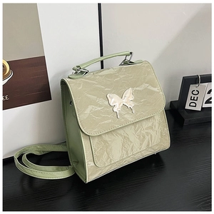 Detail of light green pleated handbag with a white butterfly buckle on a black table