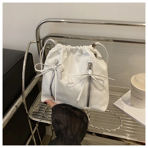Detail of white drawstring bucket bag featuring side zippers and silver chain strap