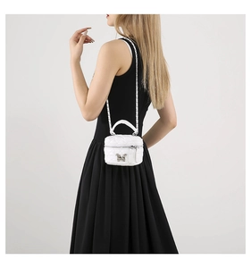 Detail of white quilted mini vanity bag featuring silver butterfly charm and chain strap