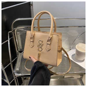 Detail of beige structured handbag with golden S-shaped logo and metallic tassel