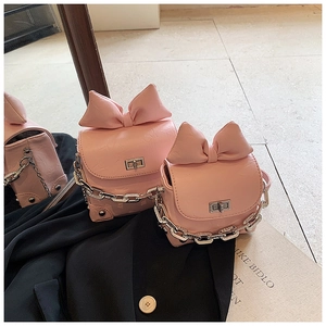 Close-up of pink leather crossbody bag with large bow and silver metal chain strap