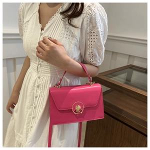 Detail of a bright magenta shoulder bag with gold round buckle and glossy leather texture