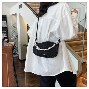 Detail of black crescent crossbody bag with decorative pearl and heart chain on model