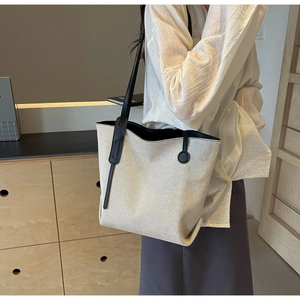 Detail of canvas tote bag with black leather straps and tassels on a model's shoulder