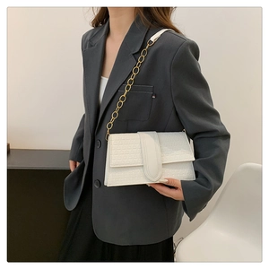 Detail of white geometric embossed flap bag with gold chain strap worn by a model