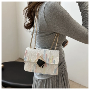 Detail view of white quilted shoulder bag featuring colorful embroidery and gold chain