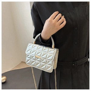 Close-up of silver quilted crossbody bag with gold hardware and woven handle detail