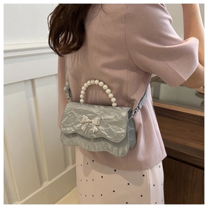 Detail of silver pleated crossbody bag with pearl handle and metal bow decoration