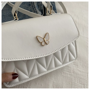 Detail einer weißen Stepptasche mit goldenem Schmetterlingsverschluss und glatter Textur