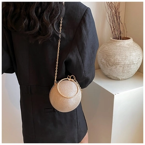 Spherical evening bag with gold glitter finish and chain strap shown on a model