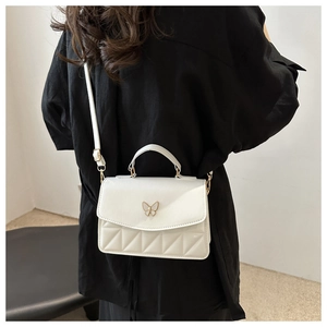 Detail of white quilted crossbody bag with golden butterfly clasp on model background