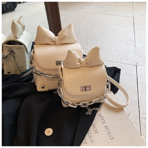 Detail of cream mini crossbody bag with a large bow decoration and silver chain strap