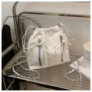 Detail of white drawstring bucket bag with dual zipper bows and silver chain strap