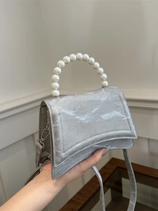 Silver metallic crossbody bag with pearl handle and hourglass base on a clean background