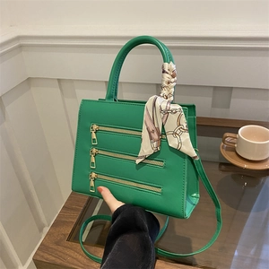 Detail of green PU leather handbag with horizontal zipper design and decorative silk scarf