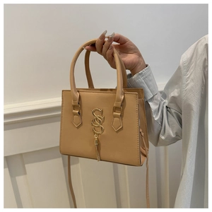 Close-up of beige handbag with gold S logo pendant, fringe tassel, and dual round handles