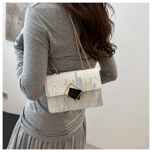 Detail view of white embroidered shoulder bag with gold chain strap on model dress