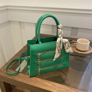 Close-up of green crossbody bag with gold zippers and decorative silk scarf handle