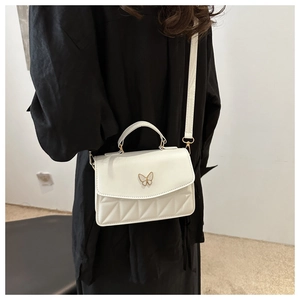 Detail of white quilted crossbody bag featuring a golden butterfly clasp and strap