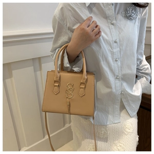 Detail of light brown leather crossbody bag with gold hardware and tassel charm
