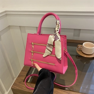 Close-up of pink leather handbag featuring triple gold zippers and a patterned silk scarf