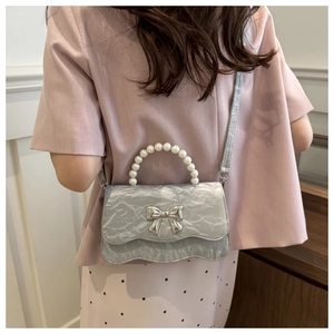Detail view of silver pleated bag with pearl handle and metal bow decoration