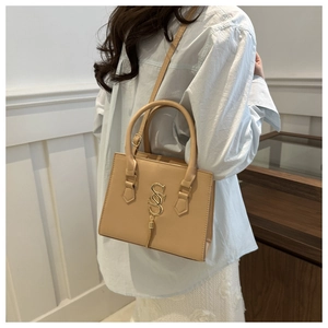 Close-up of beige handbag featuring gold S-shaped metallic buckle and elegant tassels