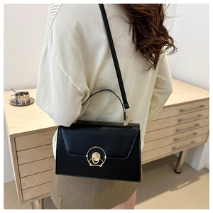 Close-up of black structured handbag featuring a gold round lock and a top handle