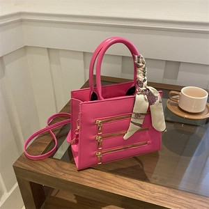 Close-up of pink crossbody bag featuring three gold zippers and silk scarf handle detail