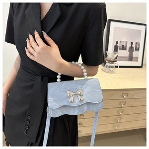 Detail of light blue crossbody bag with pearl handle and silver metal butterfly bow