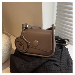Détail d'un sac besace marron foncé avec boucle ronde et charmant ours suspendu