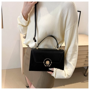 Detail of a black leather crossbody bag with a distinctive golden circular lock closure