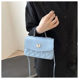 Detail of light blue quilted crossbody bag with delicate white butterfly metal clasp