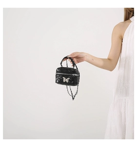 Detail of black quilted mini bag with silver butterfly clasp and leather chain strap
