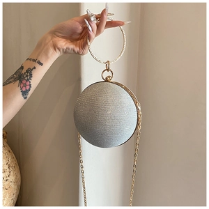 Close-up of silver spherical evening bag with glitter texture and gold metal ring handle
