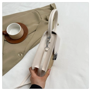 Detailed side view of structured cream handbag with brown suede panel and silver hardware