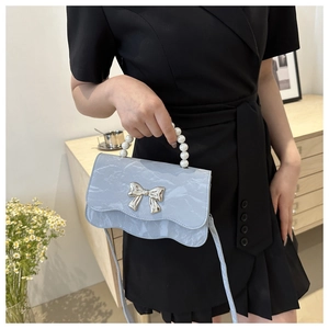 Detail of light blue pearl handle bag featuring wavy edge design and silver bow accent