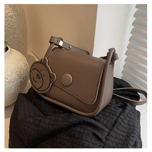 Sac bandoulière marron en cuir mat avec pendentif ours mignon sur un tissu noir