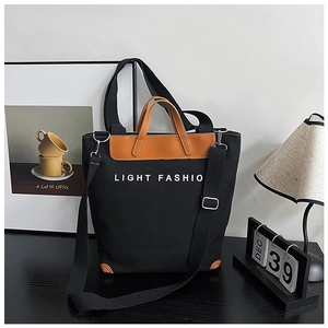 Detail view of black canvas tote bag with brown leather handles and adjustable shoulder strap