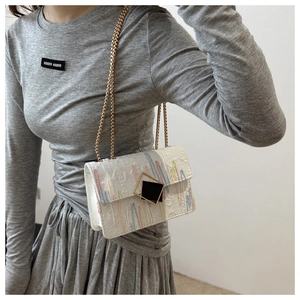 Detail der weißen strukturierten Schultertasche mit bunter Stickerei und Goldkette