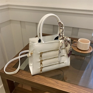 Detail of white PU leather crossbody bag with decorative gold zippers and silk scarf handle