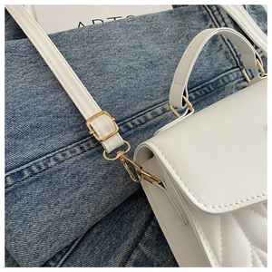 Detail der weißen gesteppten Ledertasche mit V-Nähten und goldenen Metallbeschlägen