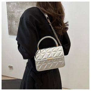 Detail of silver quilted crossbody bag with golden buckle and woven handle on model