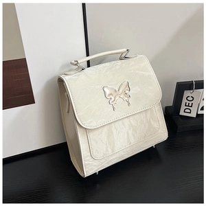 Detail view of cream-colored pleated handbag featuring a large pearl butterfly buckle