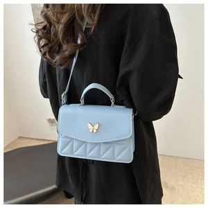Detail view of light blue quilted crossbody bag with white butterfly clasp and hand strap